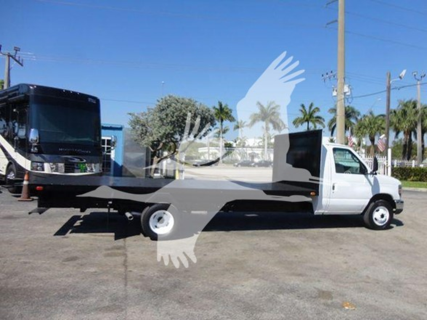 Flatbed tow truck with white cab and gray flatbed, side view.