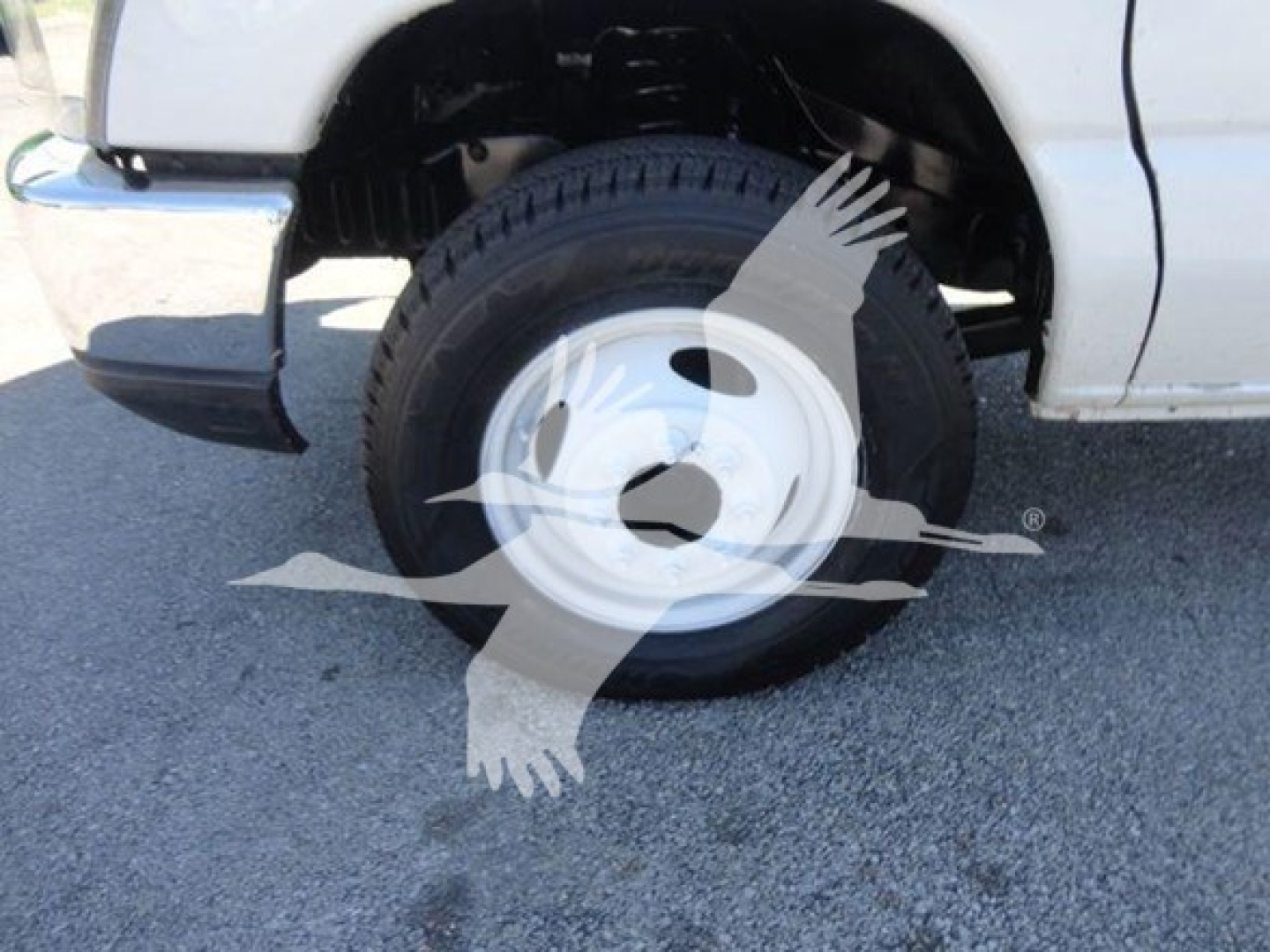 Ford E450 flatbed truck front wheel area with white steel wheel and tire, partial fender and bumper visible.