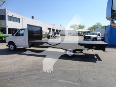 Flatbed tow truck with extended bed and low-profile side panels, white cab and flatbed on a dealership lot.