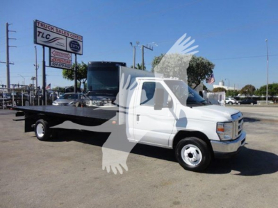 Flatbed tow truck in a dealership lot with Ford E-Series cab; visible text includes 'Truck Sales TLC' on a sign in the background and 'Ford' branding on the truck grille.