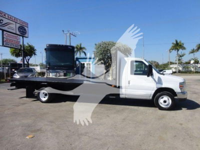 Flatbed tow truck side view showing white cab and black flatbed with a tilted loading platform on 2011 Ford E450.