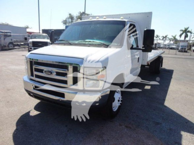 Flatbed truck showing front view of a white 2011 Ford E450 with a large chrome grille and flatbed rear.