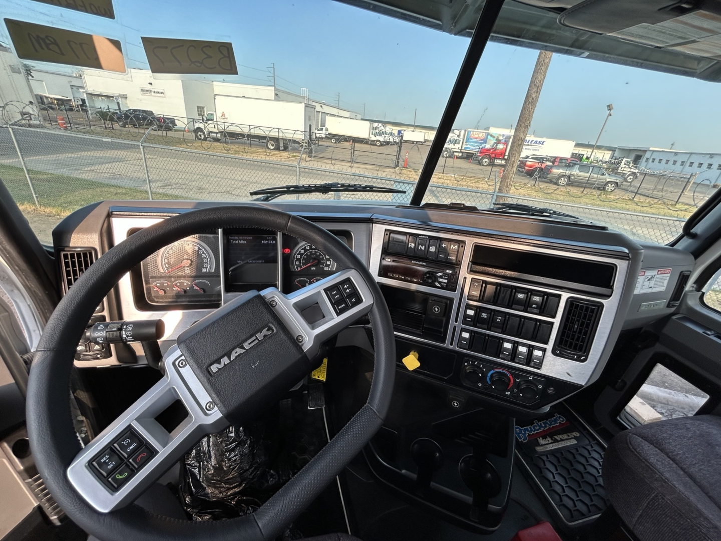 Mack GR64B truck cab interior showing steering wheel, dashboard gauges, center stack with radio and controls, driver seat, and floor mats.