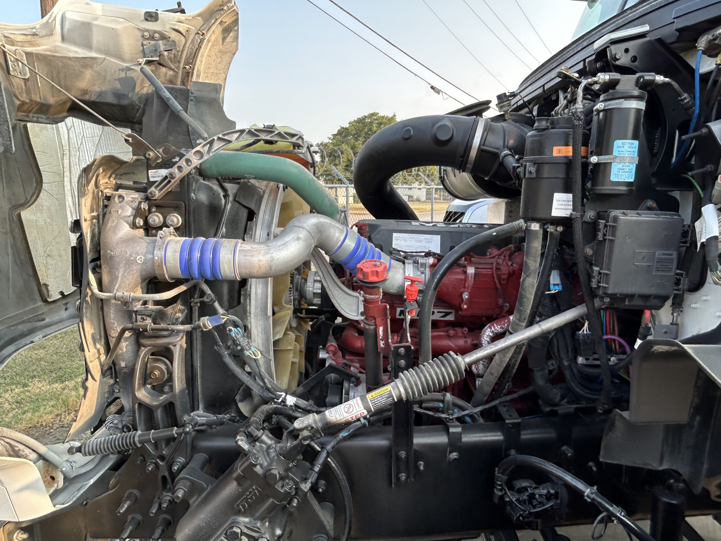Mack GR64B mixer truck engine bay showing intake hoses, turbo hoses, red engine block, black air intake with blue label, and various hoses and cables.