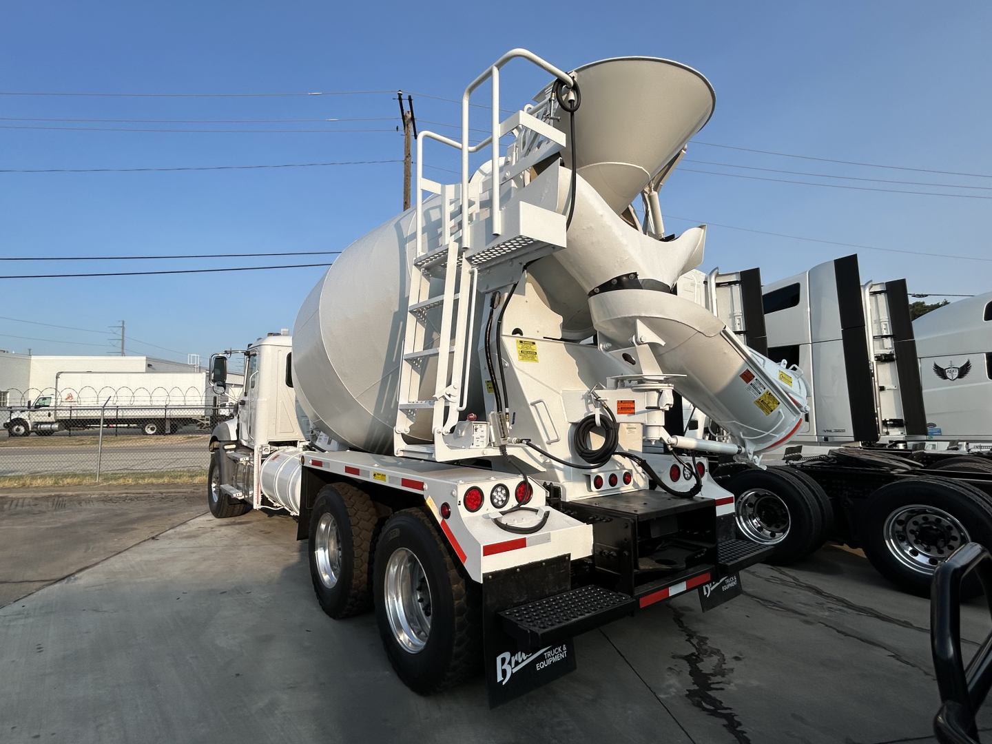 Mack GR64B mixer truck rear view showing cement loading drum and chute, rear tires, and rear access ladder.