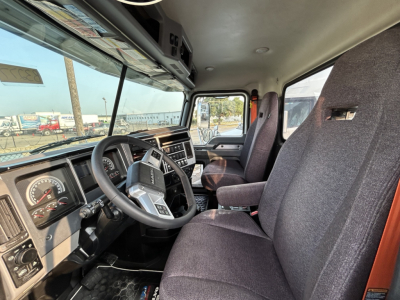 Truck cab interior showing the steering wheel, dashboard, and two front seats in a Mack GR64B mixer truck.