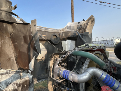 Front-left engine bay of a 2020 Mack GR64B mixer showing a green radiator hose and blue silicone coupling, exposed metal framing, and surrounding wiring.