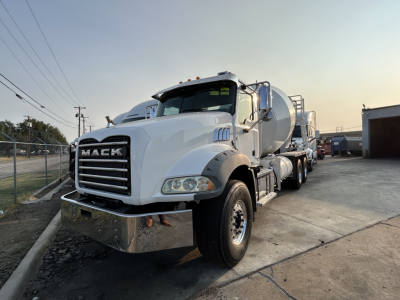 Mack GR64B mixer truck front-left view showing Mack badge on grille and chrome bumper; white cab with side mirrors and yellow warning lights; attached rear mixer body visible.