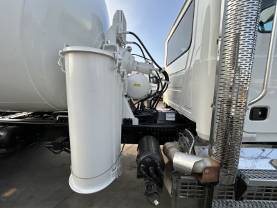 Mack GR64B mixer truck side view showing air reservoir and exhaust stack with chrome cover, hydraulic lines, and cylindrical mixer housing.