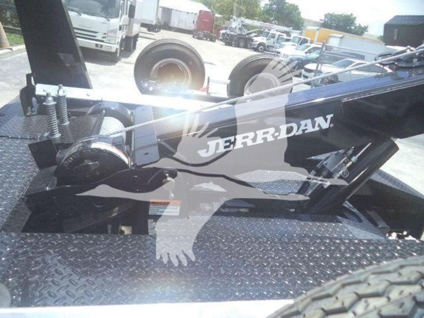 Winch truckattachment showing Jerr-Dan logo on black metal arm with diamond plate platform and dual wheels in background.