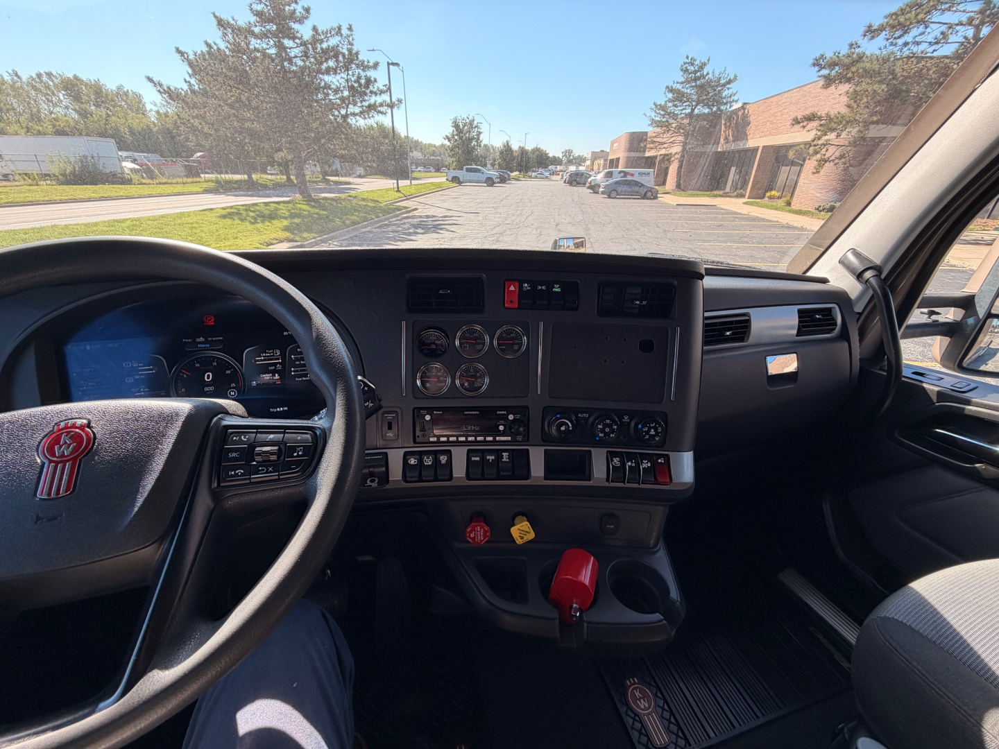 Kenworth T680 truck cockpit interior view from driver seat showing dashboard gauges, steering wheel with Kenworth logo, center controls, and gear shifter.