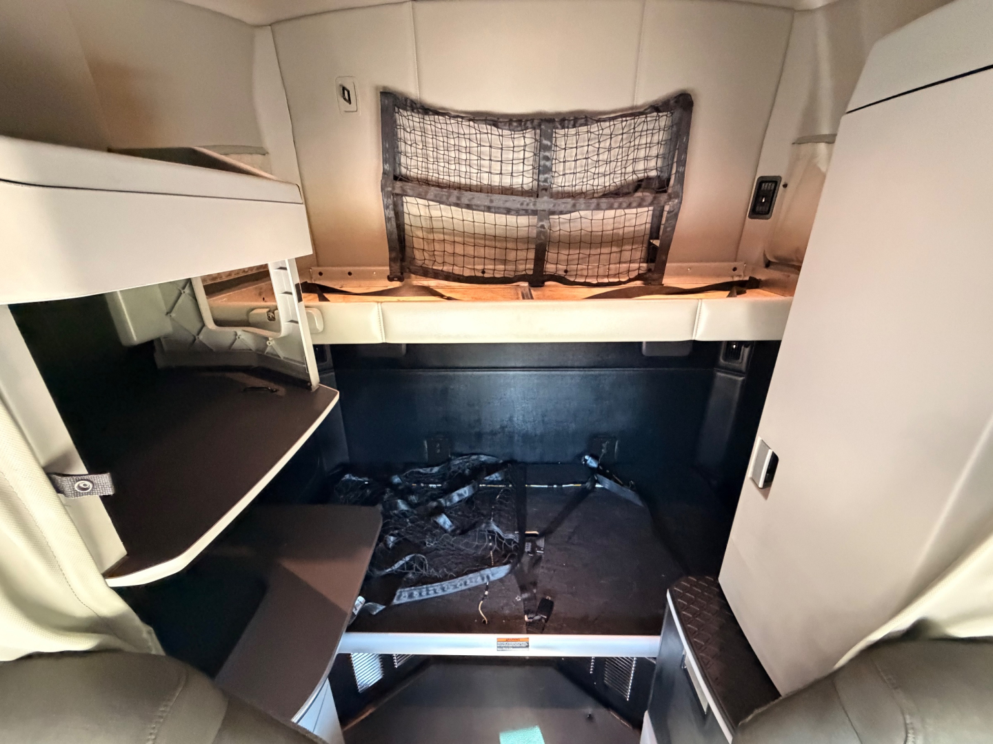 Kenworth T680 sleeper cab interior footwell with storage shelves and mesh net, view from doorway showing bunk area and floor panel.