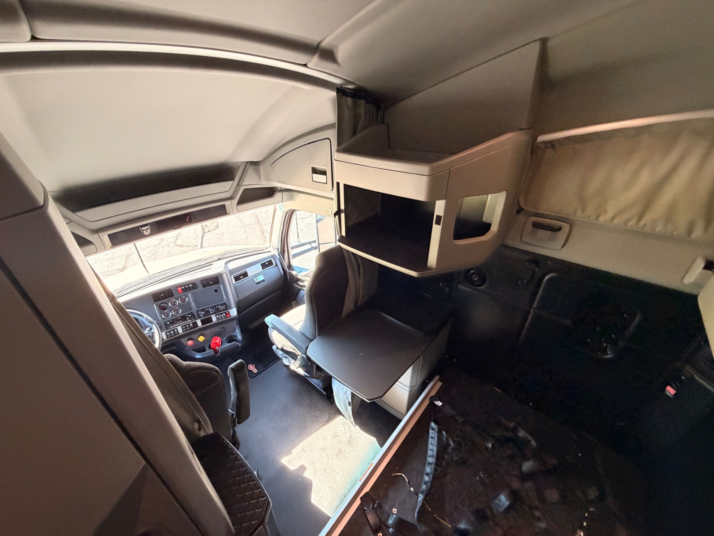 Kenworth T680 truck cab interior showing sleeper bunk area with overhead storage shelves and dashboard in view.