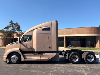 Kenworth T680 tractor with beige cab and sleeper, side view showing tandem rear axles and fuel/tank area.
