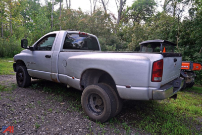 2004 Dodge Ram 3500 pickup truck in a rural setting, silver/gray with extended cab, long bed, dual rear wheels, showing rear and passenger side with a topper and some wear.