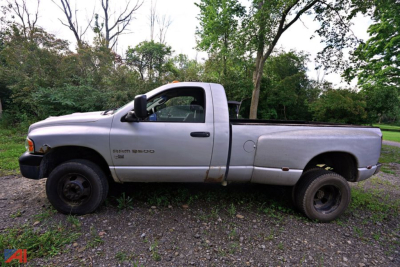 Side view of a silver 2004 Dodge Ram 3500 pickup with long bed, black steel wheels, and visible wear along the lower cab and bed.