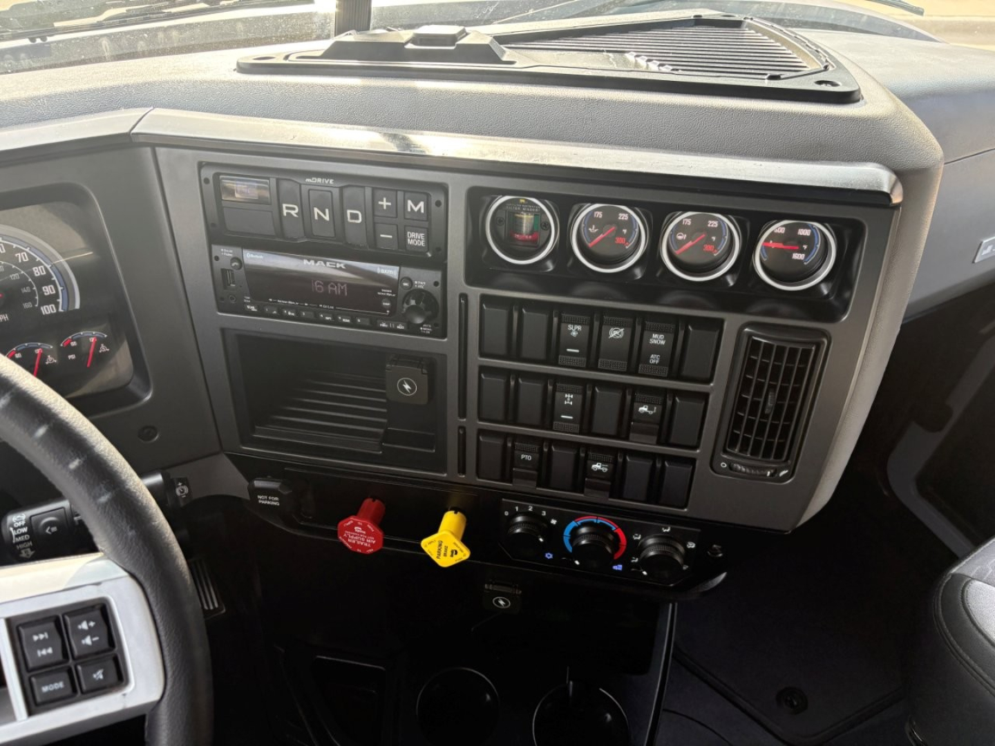 Dashboard of a Mack AN64T70 truck showing gauges, switch panels, and ignition area with steering wheel visible.