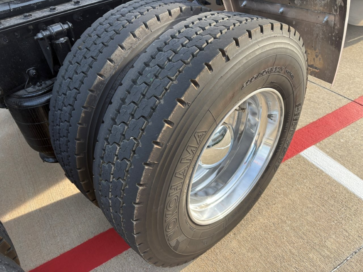 Mack AN64T70 truck engine bay/tire view showing rear dual tires with Goodyear tires and polished chrome wheel, part of a conventional sleeper truck.
