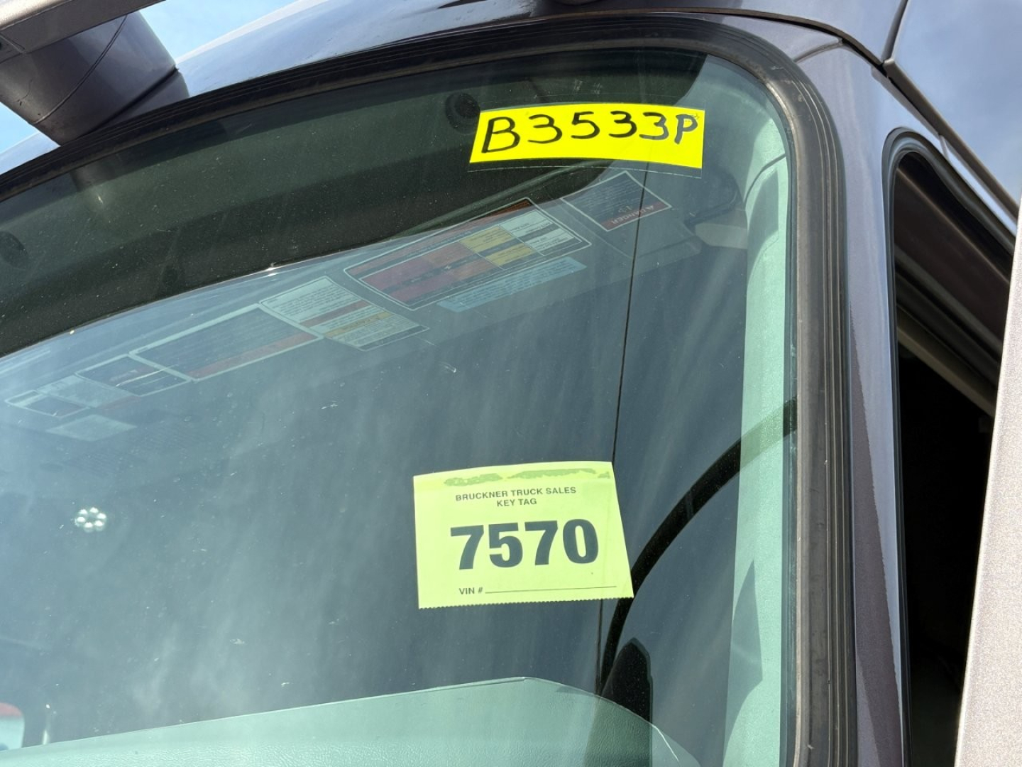 Mack AN64T70 truck window with yellow stock tag B3533P and inspection sticker showing 7570.