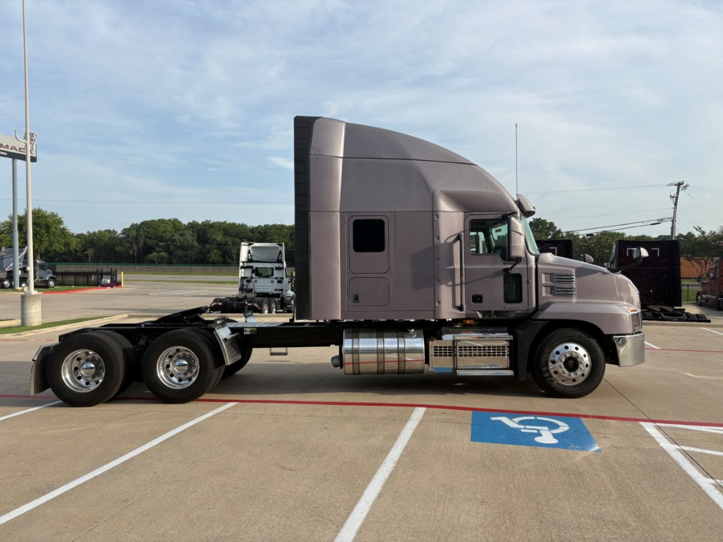 Truck cab and chassis of a 2023 Mack AN64T70 tractor in a parking lot, side view, with sleeper cab and dual rear axles.