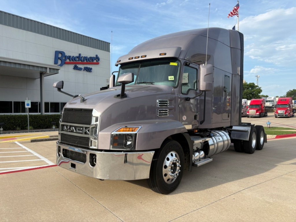 Truck: Mack AN64T70 conventional sleeper in gray parked at dealership with Bracken's Auto... in background; front grille and chrome bumper visible; VIN and stock not shown on image.