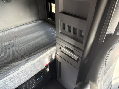 Truck cab interior with sleeper area seen; aluminum foil insulated bed area, storage compartments, and vertical control panels visible.