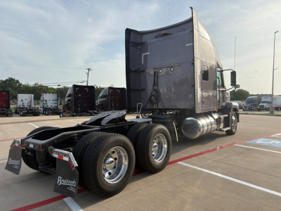 Truck rear/side view of a 2023 Mack AN64T70 conventional sleeper showing triple rear axles, fuel tanks, and cab with dark paint.