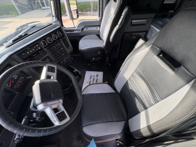 Truck cab interior showing steering wheel, dashboard with gauges, driver seat, and passenger seat in a Mack AN64T70 nighttime. Text on floor mat and control panels visible.