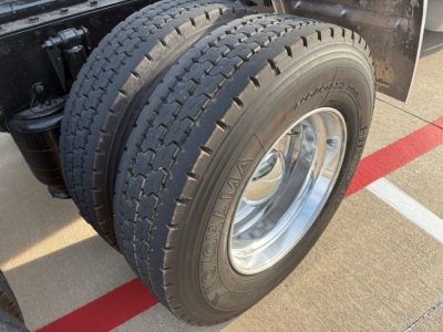 Mack AN64T70 truck engine bay/tire view showing rear dual tires with Goodyear tires and polished chrome wheel, part of a conventional sleeper truck.