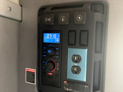 Panel view in Mack AN64T70 sleeper showing digital clock, control switches, 120V outlet, and DC/AC power panel.