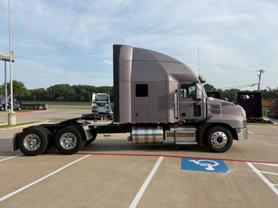 Truck cab and chassis of a 2023 Mack AN64T70 tractor in a parking lot, side view, with sleeper cab and dual rear axles.