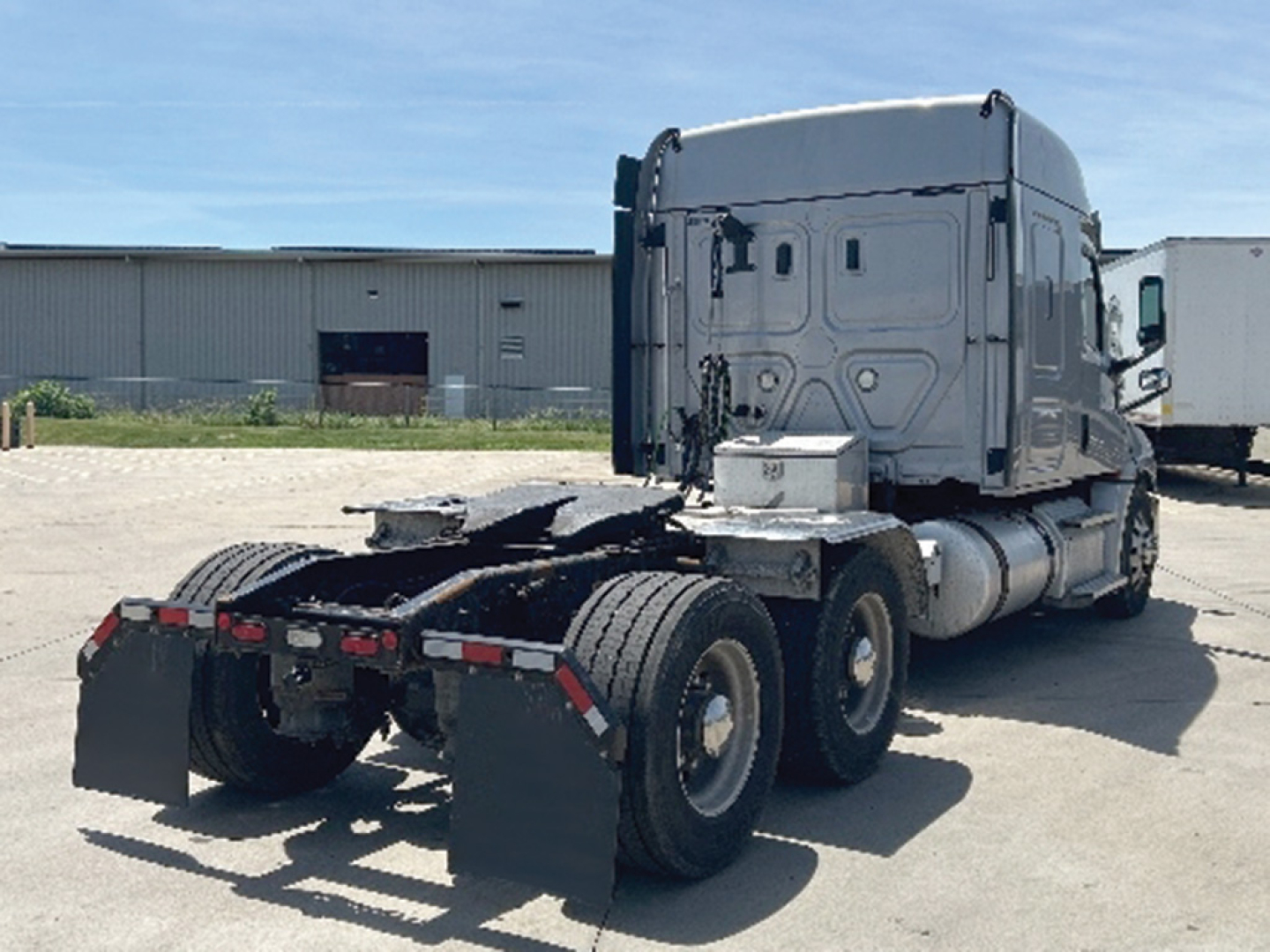 Truck chassis and cab of a Freightliner Cascadia tractor viewed from rear-right, showing sleeper cab, fuel tanks, and rear mud flaps.