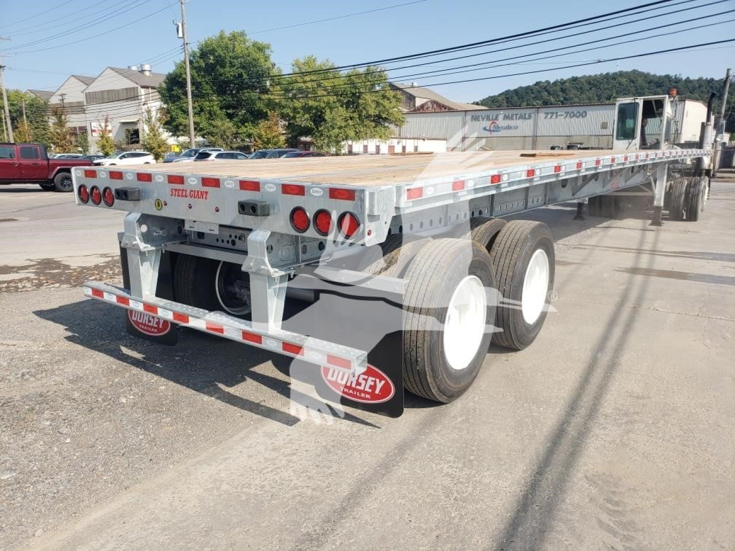 Flatbed trailer showing dual rear axles and steel bed with red and white reflective tape, Dorsey branding mud flaps, and wheel tires visible.