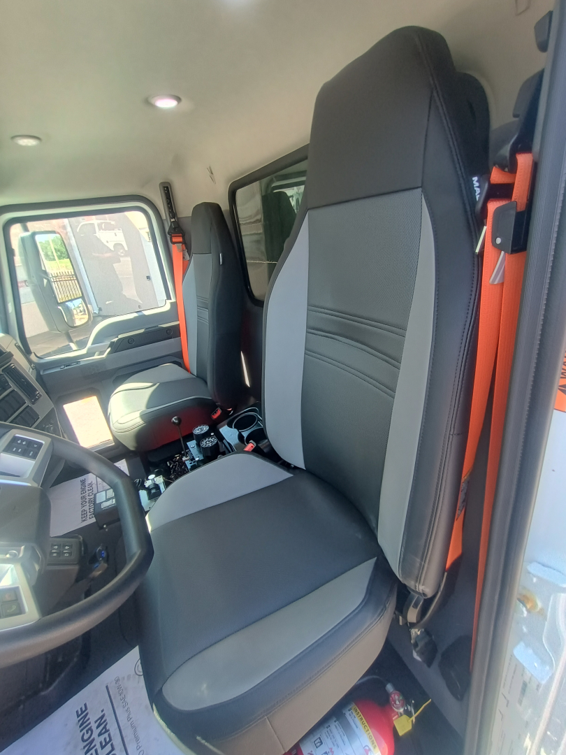 Mack MD7 truck cab interior showing driver seat and passenger seat with gray and black upholstery, steering wheel, dash, and controls visible.