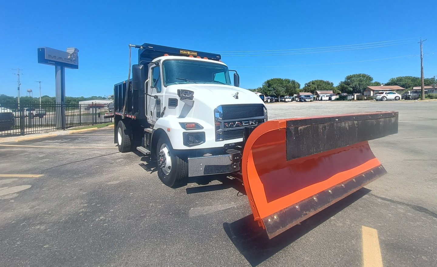 Mack MD7 truck with orange snow plow blade attached, side view in dealership lot.