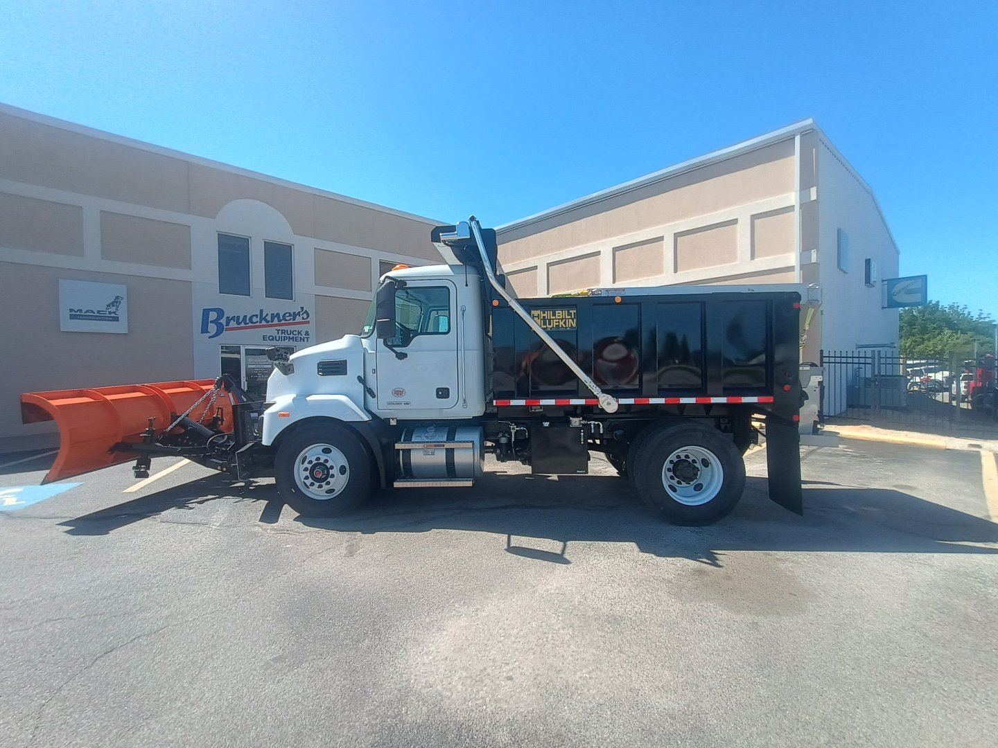 Truck with plow and dump body showing Mack MD7 cab and plow attachment, side view.