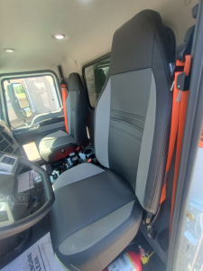 Mack MD7 truck cab interior showing driver seat and passenger seat with gray and black upholstery, steering wheel, dash, and controls visible.