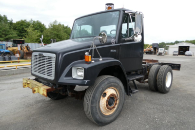 Truck cab and chassis showing Freightliner FL70 chassis with dual rear axles, steel wheels, front bumper, and side mirrors.
