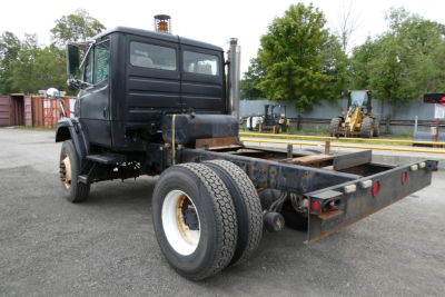 2004 Freightliner FL70 cab and chassis rear view showing dual rear wheels, flatbed chassis, and exhaust stacks.