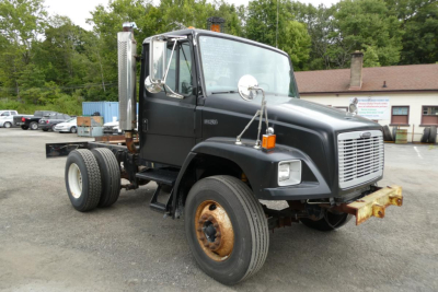Truck cab and chassis showing Freightliner FL70 with black cab, front grille, side mirrors, and dual rear wheels; visible rust on rear wheel and front bumper; no visible license plate