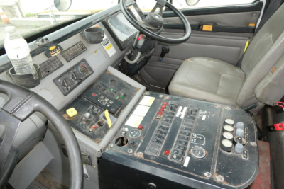 Cab interior of a 2004 Freightliner FL70 showing dashboard with switches, steering wheel, control panel, and two cup holders; a water bottle rests in a holder left of the steering wheel.