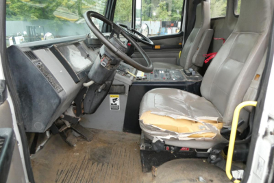 Cab and Chassis truck interior showing steering wheel, dashboard, and worn driver seat with torn upholstery; overall rugged cab with exposed pedals and floor mat.