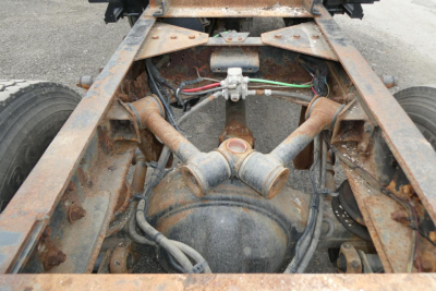 Truck chassis rear view showing driveline and frame rails, axle housing, suspension components, and rust-orange metal framing under Freightliner cab and chassis.