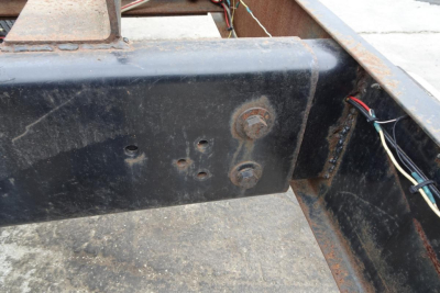 Freightliner FL70 chassis frame showing mounting bolts and wiring bundle on a black painted metal surface.