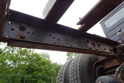 Chassis frame rail showing bolted holes and rust spec under a Freightliner cab and chassis, wheel and suspension components visible at right.