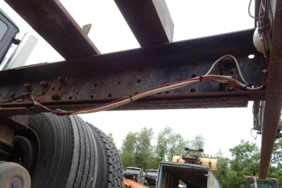 Chassis frame showing rusted I-beam with wiring harnesses and a wheel in the foreground, used Freightliner FL70 chassis image.