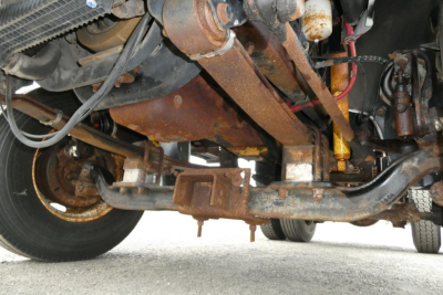 Underneath view of a Freightliner FL70 cab and chassis showing rusted frame rails, suspension, driveshaft, and steering linkage.