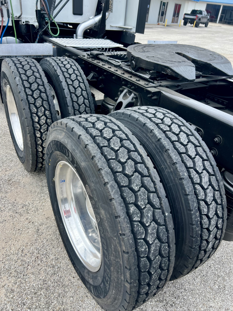 Trucks suspension area with dual rear axles and heavy-duty tires on a Kenworth truck chassis showing wheel rims and undercarriage components.