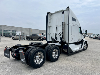 Kenworth T680 tractor cab with sleeper, rear dual axles, white exterior, visible fifth wheel and undercarriage in a truck lot.