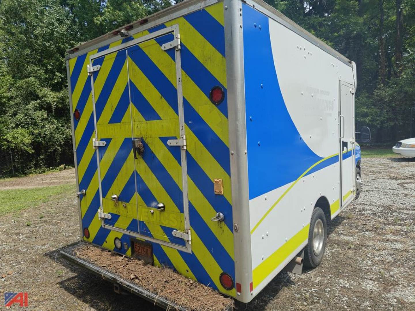 Rear and side view of a white Ford E-350 cargo van conversion with bright blue and yellow chevron rear pattern and reflective strips.
